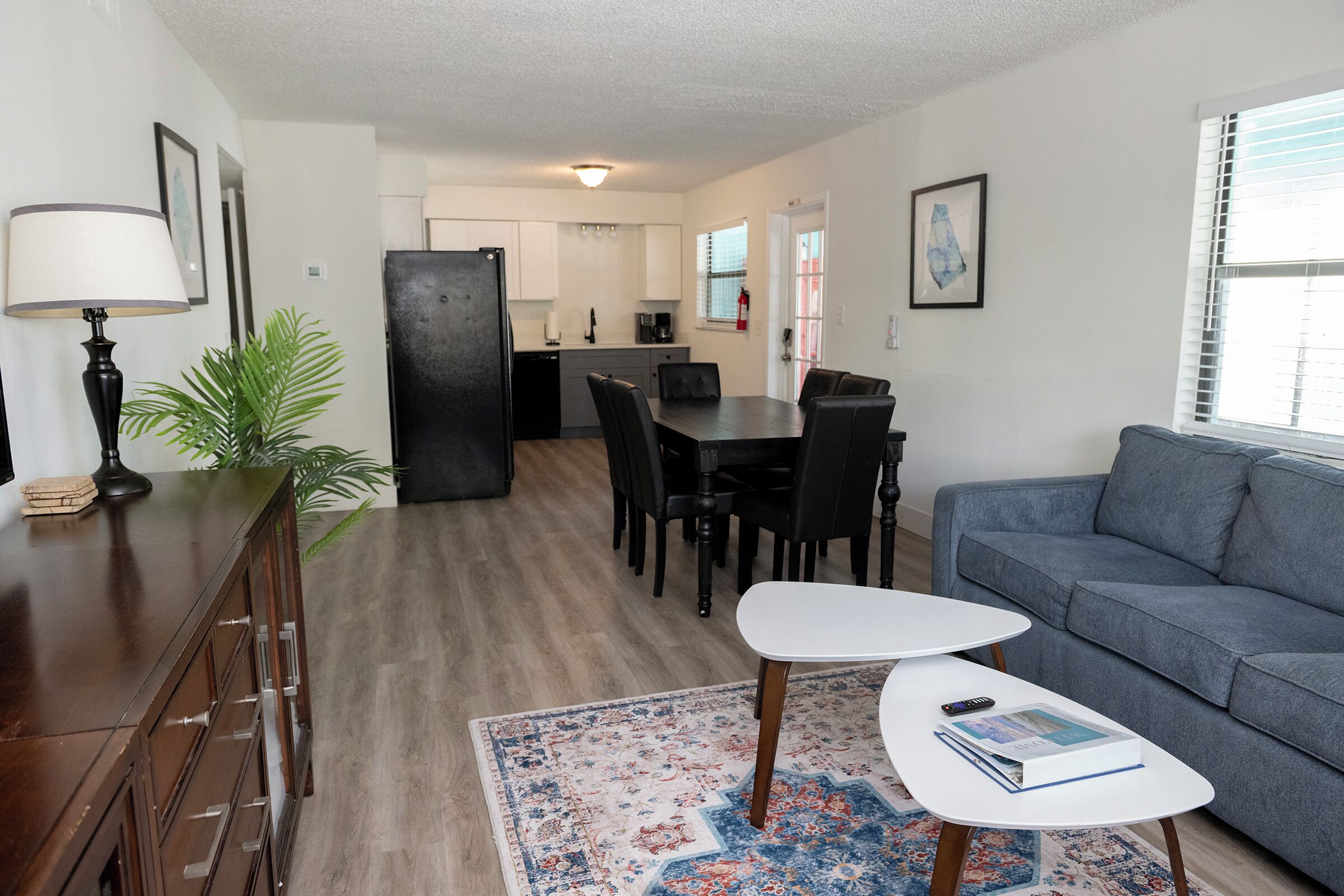 A modern living room with a sofa, a dining table with chairs, a coffee table, and a kitchen area in the background.