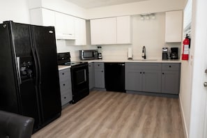 A kitchen with white cabinets, a black refrigerator, a microwave, a coffee maker, and a dishwasher.