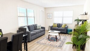 Un salon avec un canapé gris, une table à manger avec des chaises, une table basse et une plante en pot.