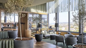A modern hotel lobby with large windows, seating areas, and potted plants. - Crystalbrook Kingsley (Newcastle)