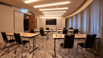A conference room with multiple tables and chairs, a large screen, and a carpeted floor.