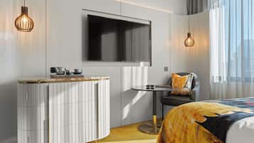 A modern hotel room with a large bed, a small round table, a TV mounted on the wall, and a minibar.