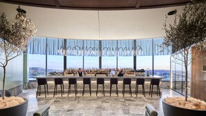 A modern bar area with a long counter, multiple bar stools, and large planters. - Crystalbrook Kingsley (Newcastle)