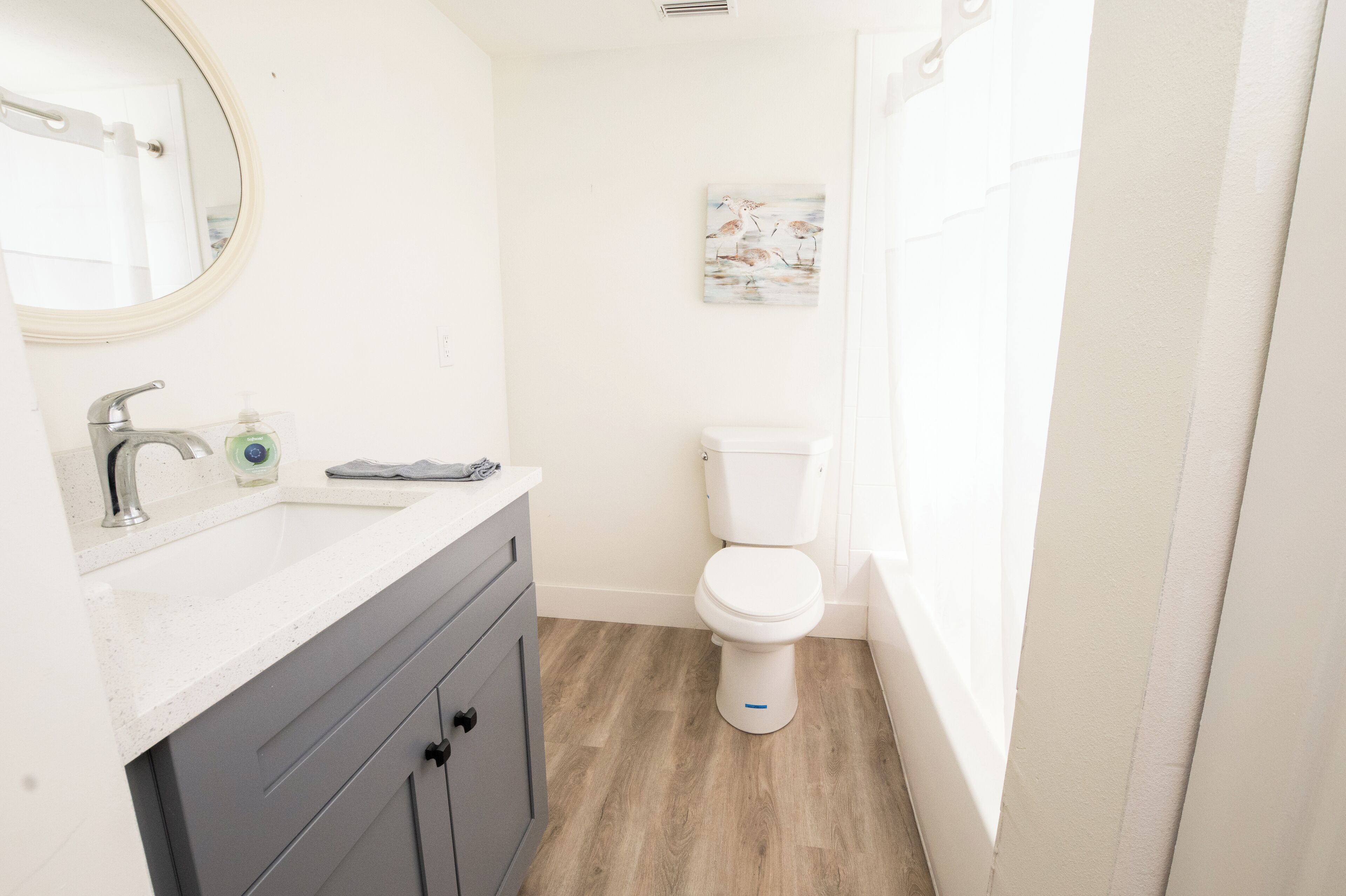 Une salle de bain avec un lavabo blanc, un miroir, des toilettes et un plancher en bois.