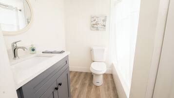 Une salle de bain avec un lavabo blanc, un miroir, des toilettes et un plancher en bois.