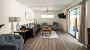 Un salon comprenant un canapé, une table basse, une lampe, un ventilateur de plafond et une porte-fenêtre coulissante.