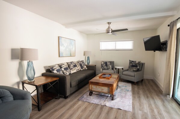 A living room with a sofa, armchair, coffee table, lamp, and a ceiling fan.