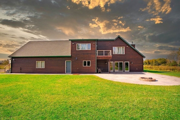 A two-story wooden house with a covered porch, a fire pit, and a well-maintained lawn.