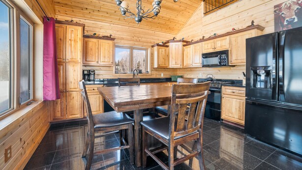 Eine Holzhütte mit einer Küche, einem Esstisch, Stühlen, einem Kühlschrank und einer Mikrowelle.