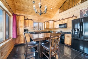 A wooden cabin kitchen with a dining table, chairs, a refrigerator, and a microwave.