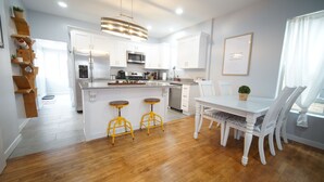 A modern kitchen with white cabinets, a central island with stools, and a dining table with chairs.