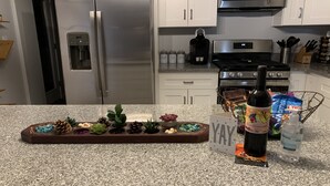 A kitchen with a granite countertop, stainless steel appliances, and a variety of decorative items including a tray with pinecones and succulents.