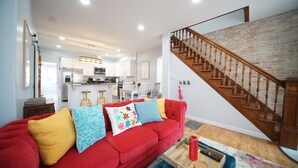 A modern living room with a red sofa, wooden staircase, and a kitchen in the background.