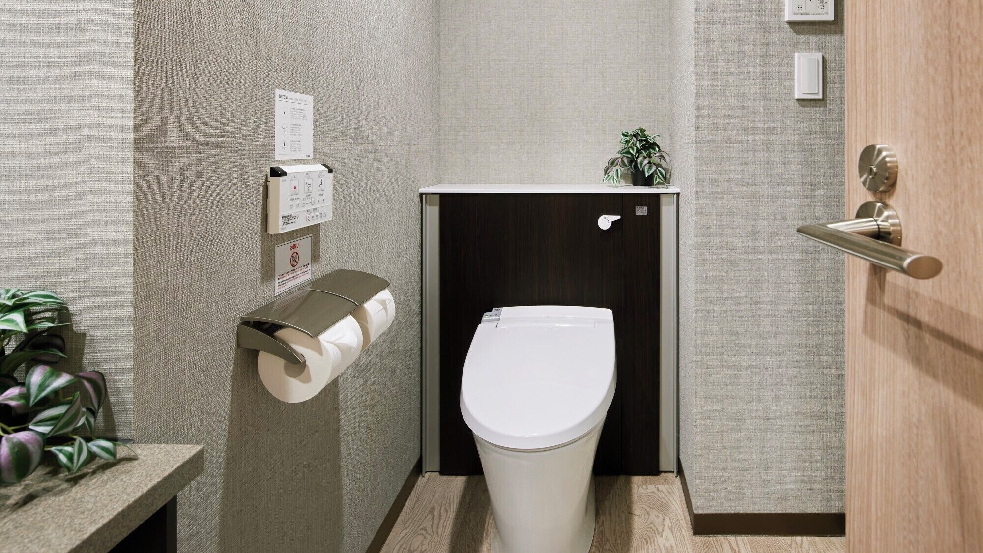 A compact bathroom with a toilet, paper dispenser, and a small potted plant.