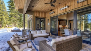 A covered outdoor seating area with wicker furniture and a stone fire pit. - Bound to Impress. Private Hot Tub, Golf Access & Exclusive Club Amenities! (Truckee)