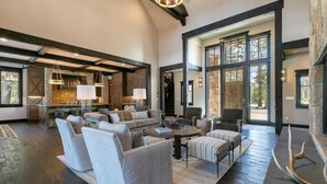 A spacious living area with a stone fireplace, large windows, and a high ceiling with exposed beams. - Bound to Impress. Private Hot Tub, Golf Access & Exclusive Club Amenities! (Truckee)