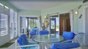 A room with a glass table surrounded by blue chairs, a small table with a vase, and a view through a glass door. - BEACH and POOL at Rum Point - North Side in most secluded and tranquil area (North Side)