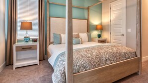 Un lit à baldaquin à quatre poteaux, surmonté d’une couvre-lit à motifs, avec des tables de chevet dotées de lampes, une fenêtre avec des stores et une porte.