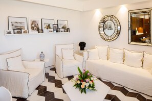 A modern living room with a white sofa set, a coffee table with a floral centerpiece, and framed pictures on the wall.
