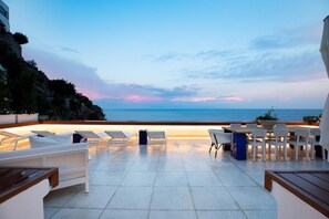 En udendørs terrasse med loungesæder og spiseplads med udsigt over havet.