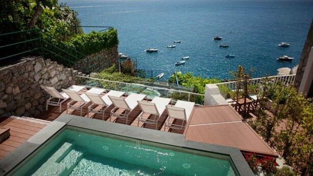A pool area with lounge chairs overlooking the sea, a stone wall, and a wooden deck. - Amalfi Coast Luxury Villa with Swimming Pool (Praiano)