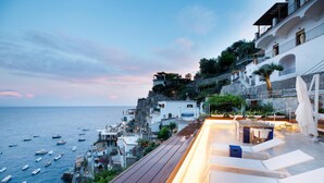 A coastal terrace with outdoor seating and a view of the sea and buildings. - Amalfi Coast Luxury Villa with Swimming Pool (Praiano)