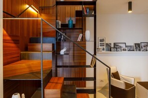 Eine moderne Treppe mit Holzvertäfelung und Metallgeländern, die zu einer Sitzecke mit einem weißen Sofa und einem Couchtisch führt.