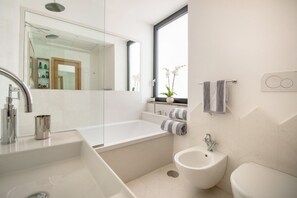 Une salle de bain moderne avec un grand miroir, une baignoire, un bidet et des toilettes.