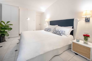 Une chambre à coucher bien rangée, avec un lit, des tables de chevet, une commode, une lampe, une plante en pot et une porte.