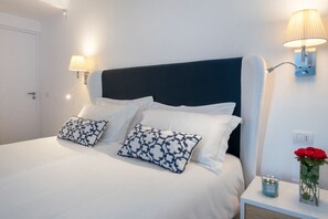 A neatly made bed with white bedding and two patterned pillows, a bedside table with a candle and a vase of flowers, and wall-mounted lamps. - MyExclusiveItaly - Luxury Apartment with Penthouse and Pool (Sant'Agnello)