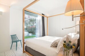 Un dormitorio moderno con una cama grande, una silla, una mesita de noche con una lámpara y vistas al exterior.