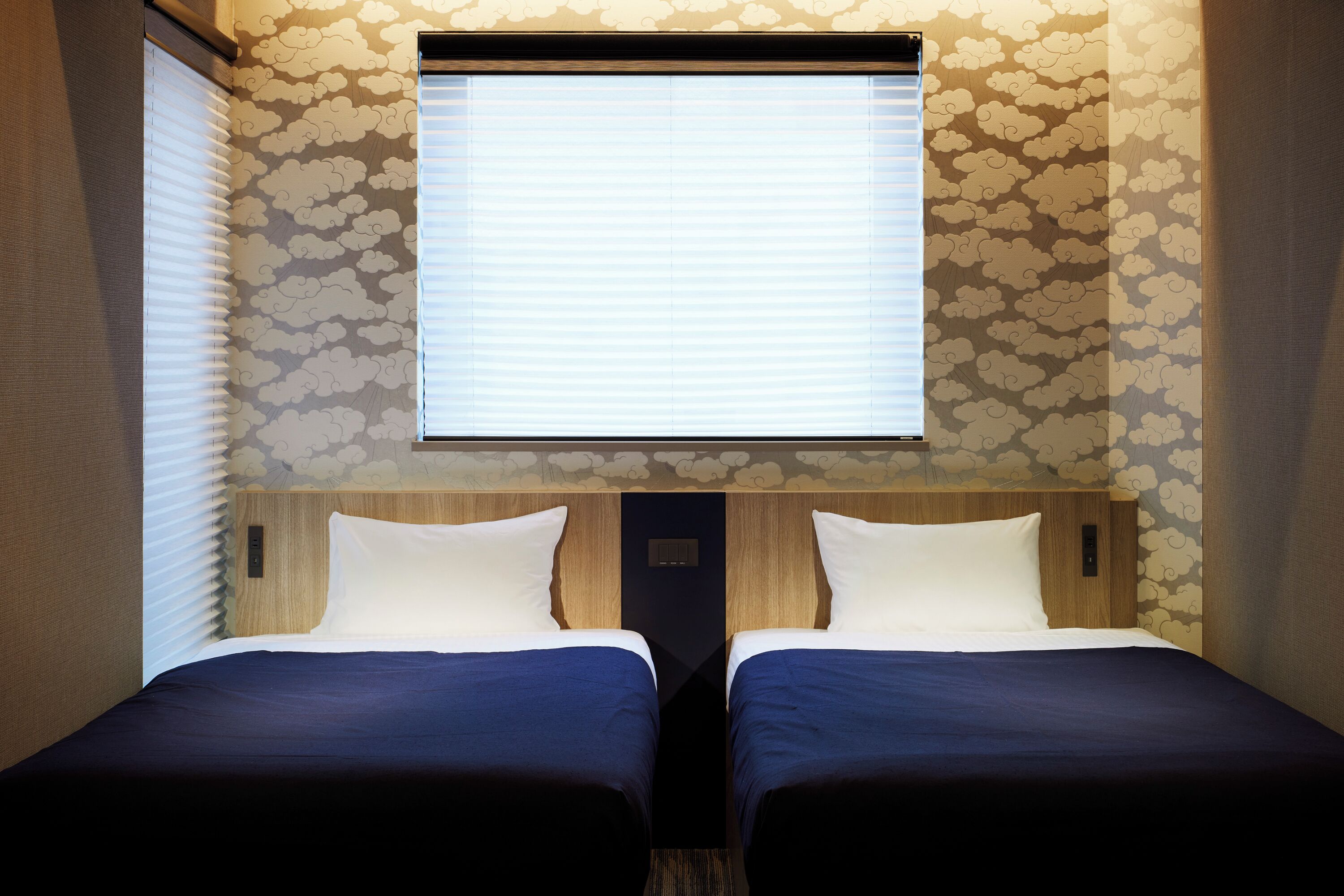 A room with two beds, a window, and a wall with a cloud pattern.