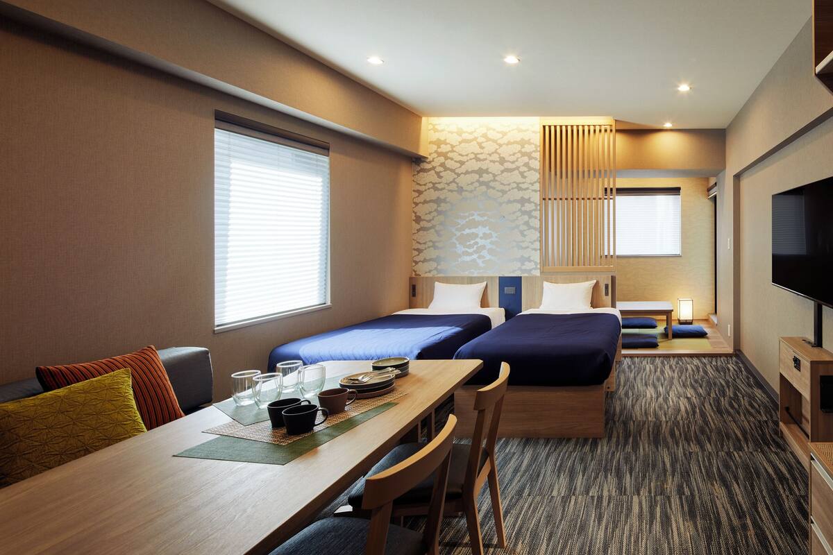 Ein Hotelzimmer mit zwei Betten, einem Esstisch und einem Fernseher.