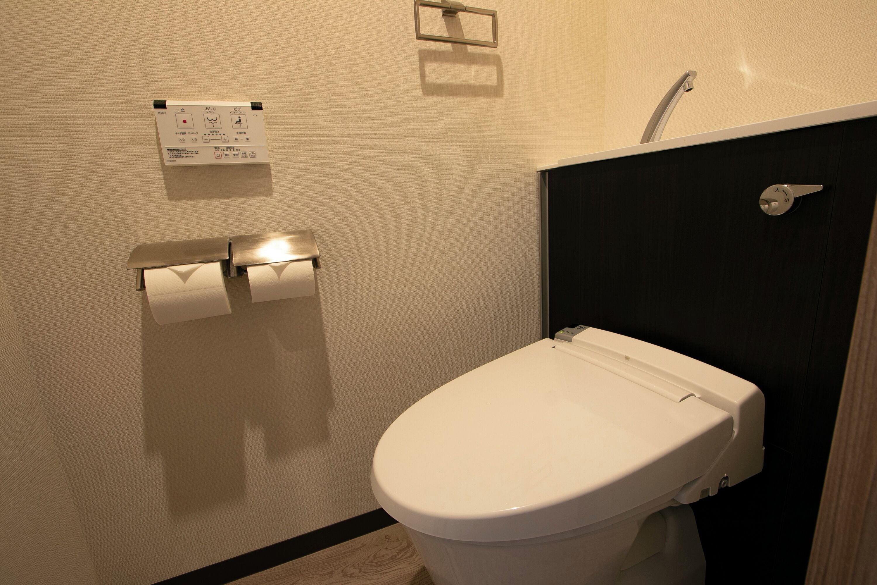 Des toilettes blanches, un mur noir et un petit panneau de commande situé juste au-dessus.