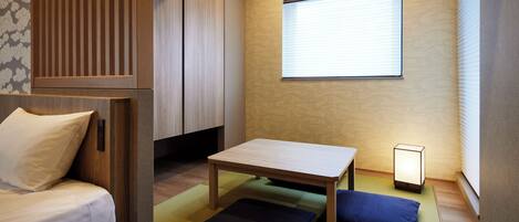 Una habitación pequeña con cama, una mesita y una ventana con persianas.