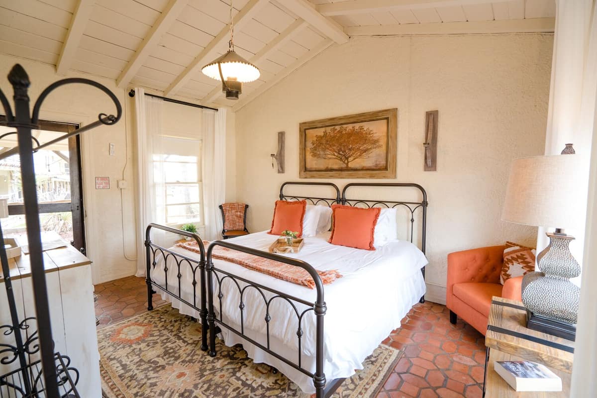 Un dormitorio con una cama, una silla, una lámpara y un cuadro en la pared.
