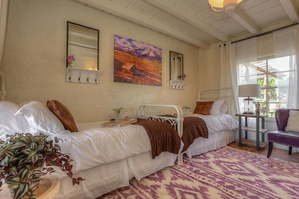 Un dormitorio con dos camas, un cuadro grande, un espejo y una ventana con cortinas.