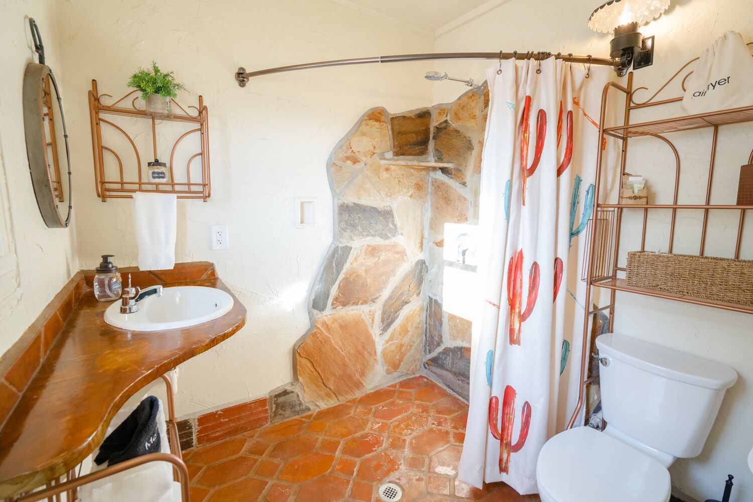 A bathroom with a stone shower enclosure, a wooden vanity with a sink, and a white toilet.