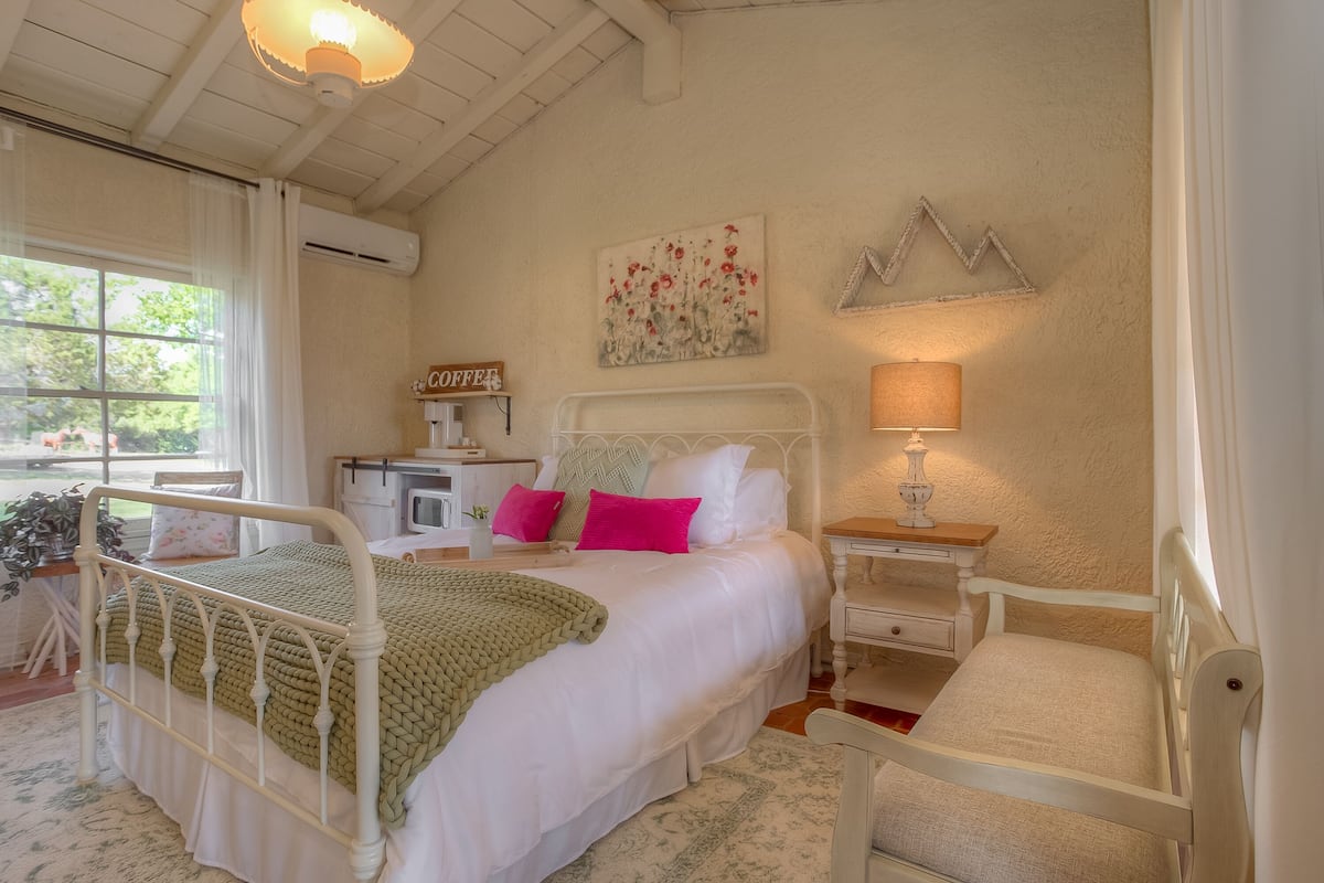 Un dormitorio con cama, mesita de noche, lámpara y un cuadro en la pared.