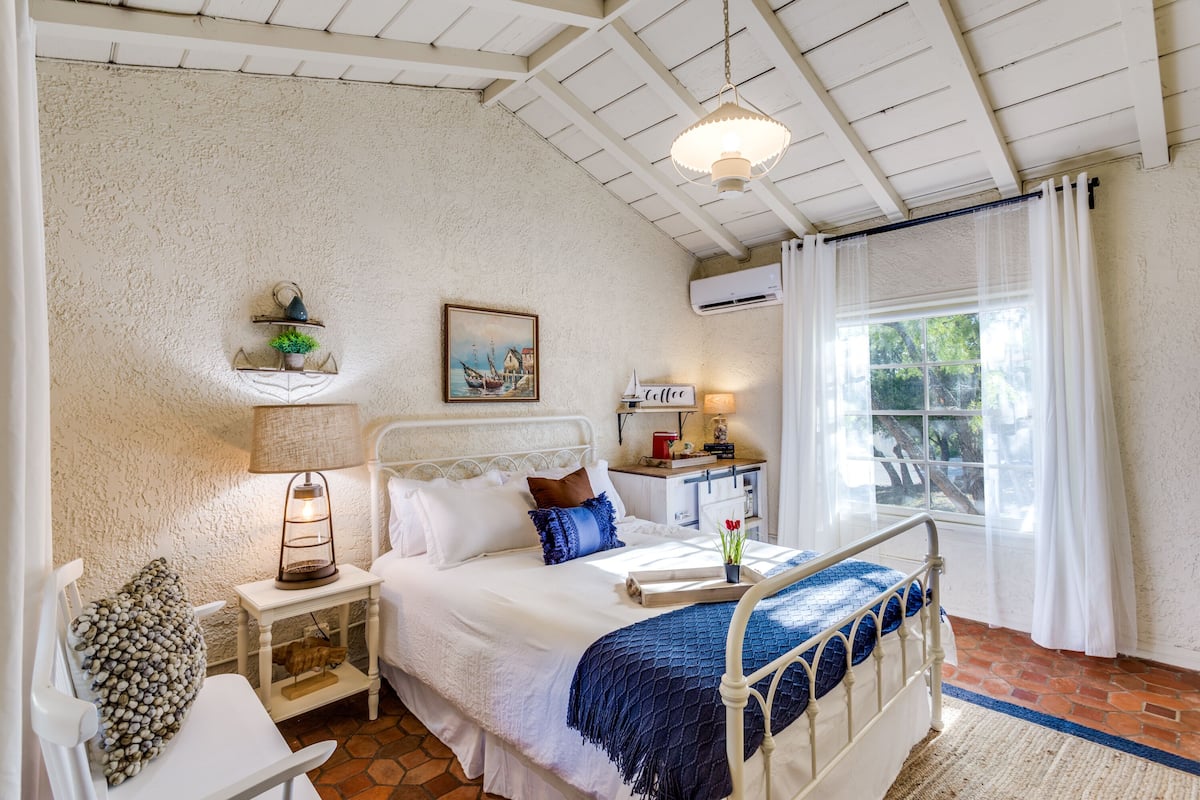 Un dormitorio con cama, mesita de noche, lámpara y ventana con cortinas.