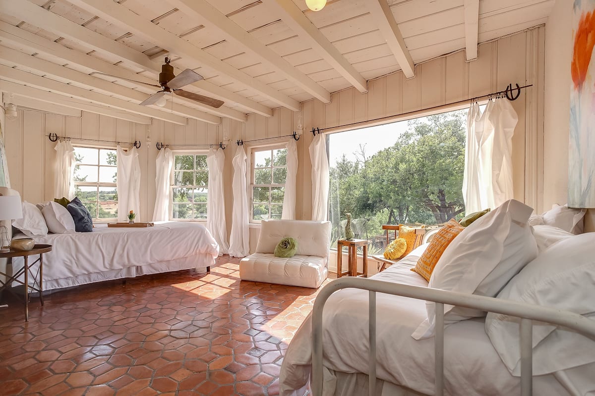 Un dormitorio con cama, sofá, una mesita y una ventana con cortinas.