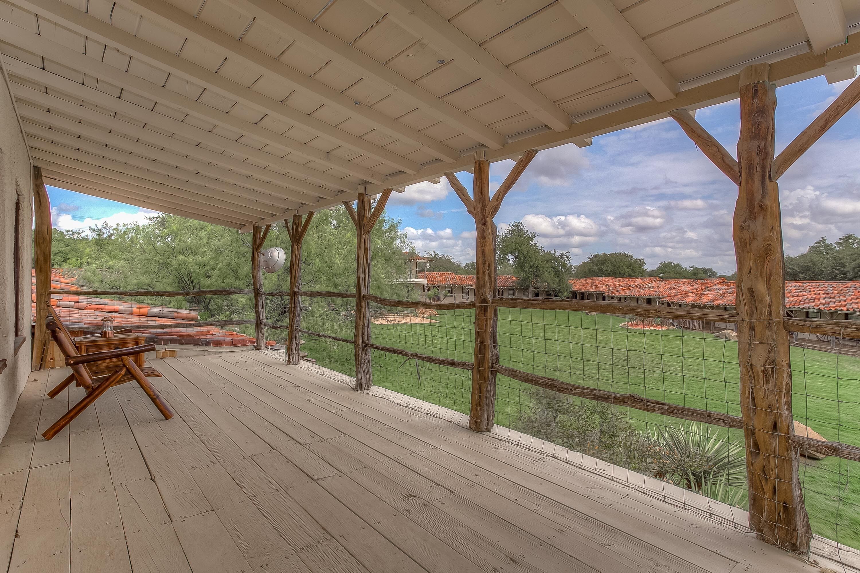 A covered outdoor area with a wooden deck, a table with chairs, and a view of a baseball field.