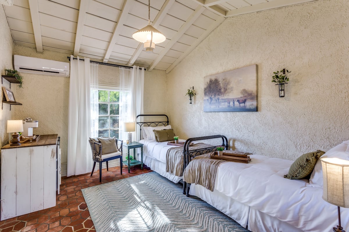 Un dormitorio con dos camas, un escritorio, una silla, una alfombra y un cuadro en la pared.