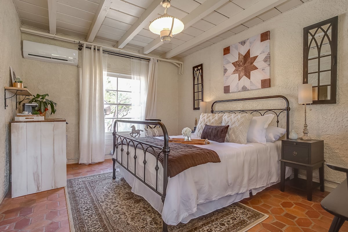 Un dormitorio con cama, mesita de noche, lámpara y ventana con cortinas.