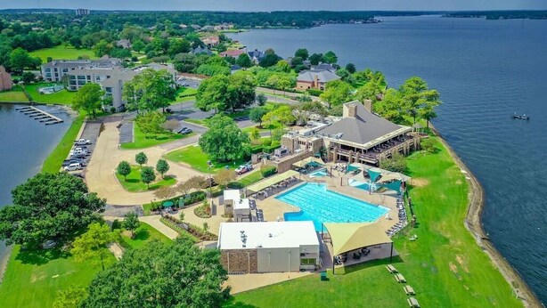 Una vista aerea di un resort con una grande piscina, un campo da tennis e un porto turistico.