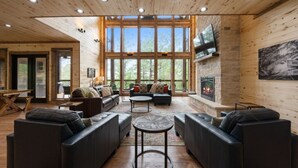 Amplia sala de estar con sofás de cuero, chimenea y grandes ventanales con vistas al exterior.