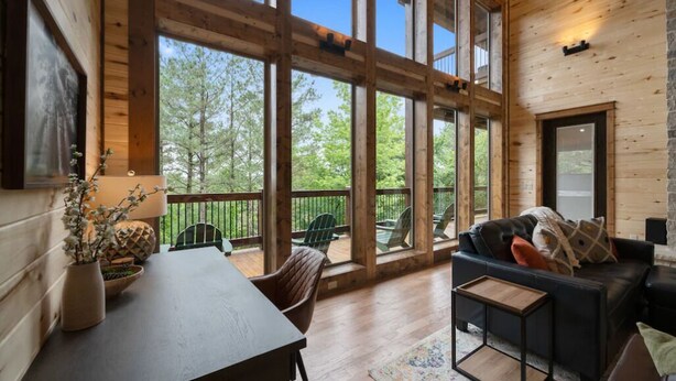Una habitación amplia con un gran ventanal, una terraza de madera, un sofá y una mesa.