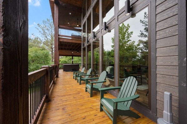 Una terraza de madera con sillas Adirondack, una parrilla y un ventanal con vistas a una zona boscosa.