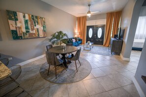 A dining area with a round table and chairs, a sofa, a TV stand, and a door with curtains.