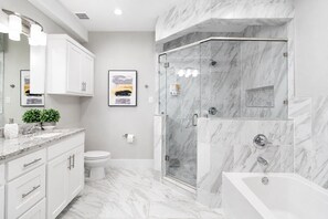 Une salle de bain moderne équipée d’une douche, de toilettes et d’une baignoire, avec des carreaux de marbre et des meubles blancs.